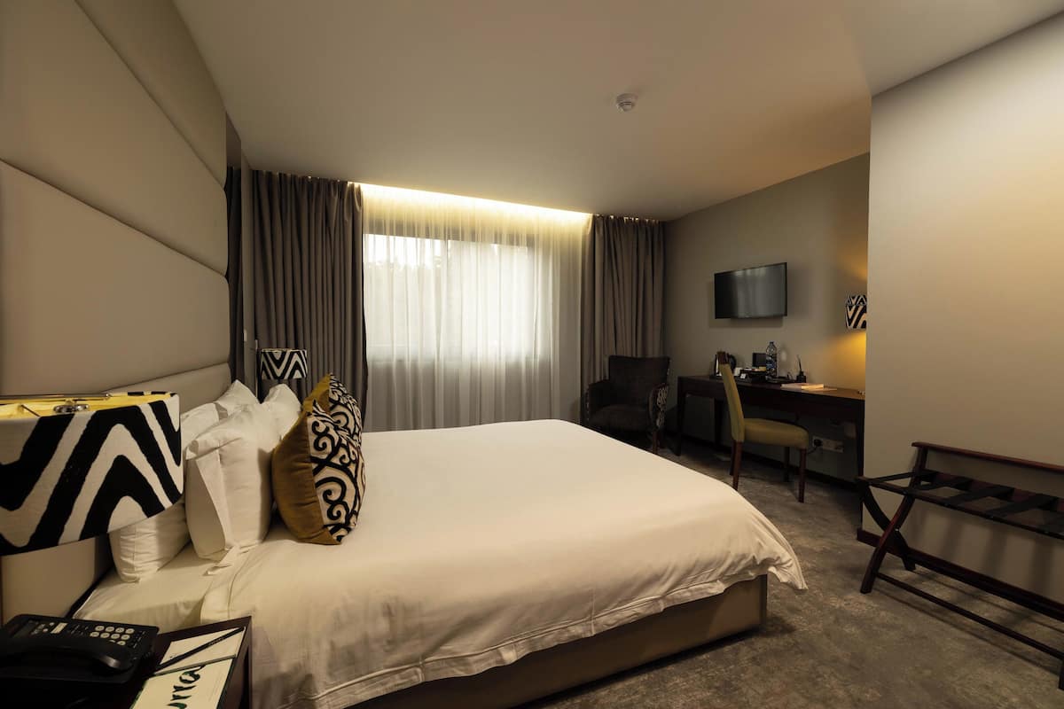A hotel room with a large bed, a desk, a chair, a television, and a window with curtains.