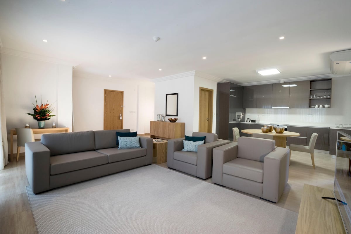 A modern living room with a grey sectional sofa, a small coffee table, and a dining area with a round table and chairs.