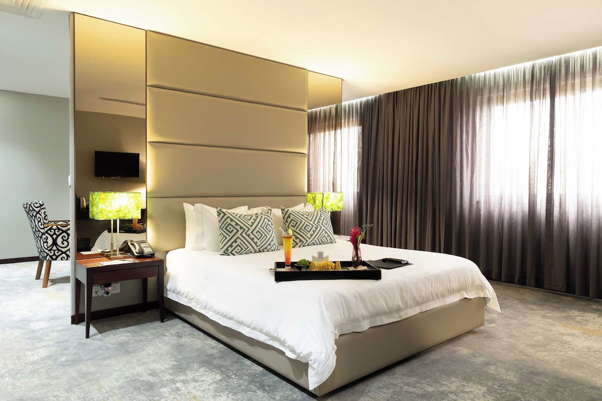 A hotel room with a large bed, a bedside table with a lamp, a tray with snacks and a drink, and a TV on the wall.