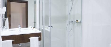 Un baño moderno con ducha de vidrio, un lavamanos blanco y encimera de madera, y un espejo grande.