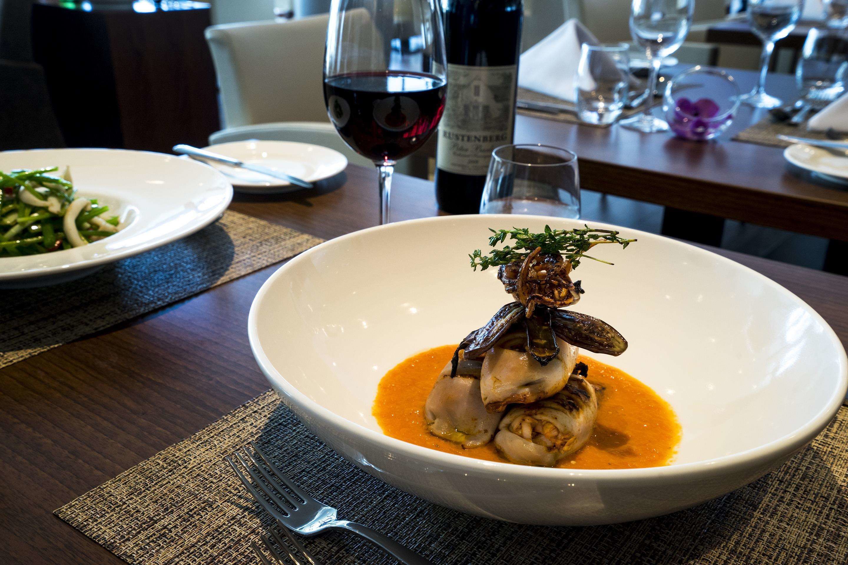 A dining table with a white bowl containing a seafood dish, a wine bottle, and glasses.