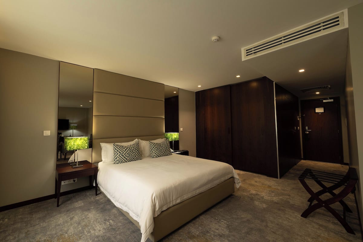 A modern bedroom with a large bed, a nightstand, a mirror, and a wardrobe.