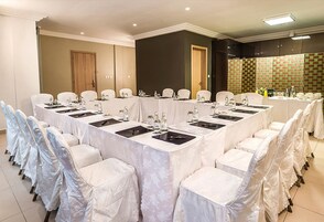 A conference room with a long table, white chairs, and a tiled floor.