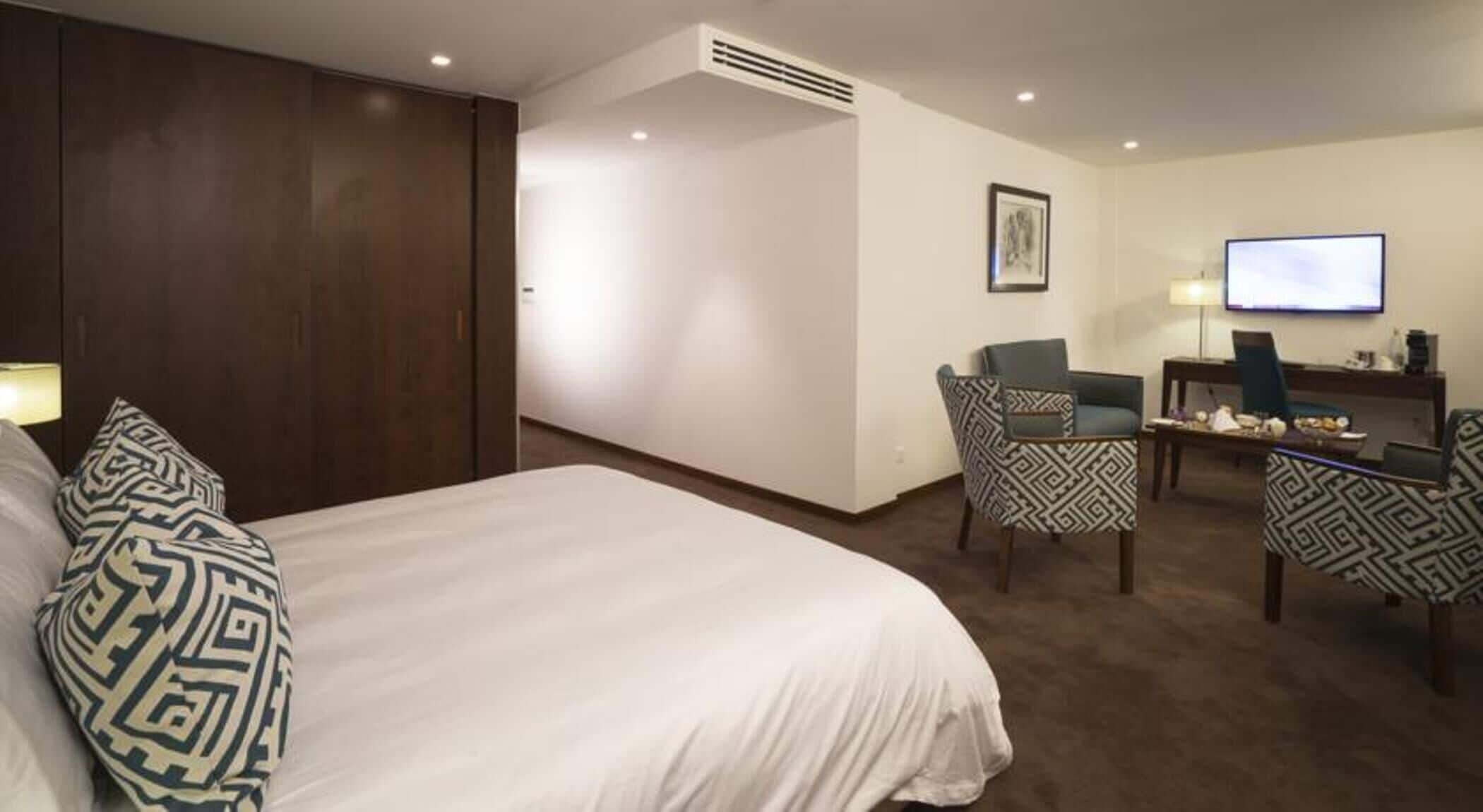 A hotel room with a large bed, a desk with a chair, a television, and a wall-mounted picture.