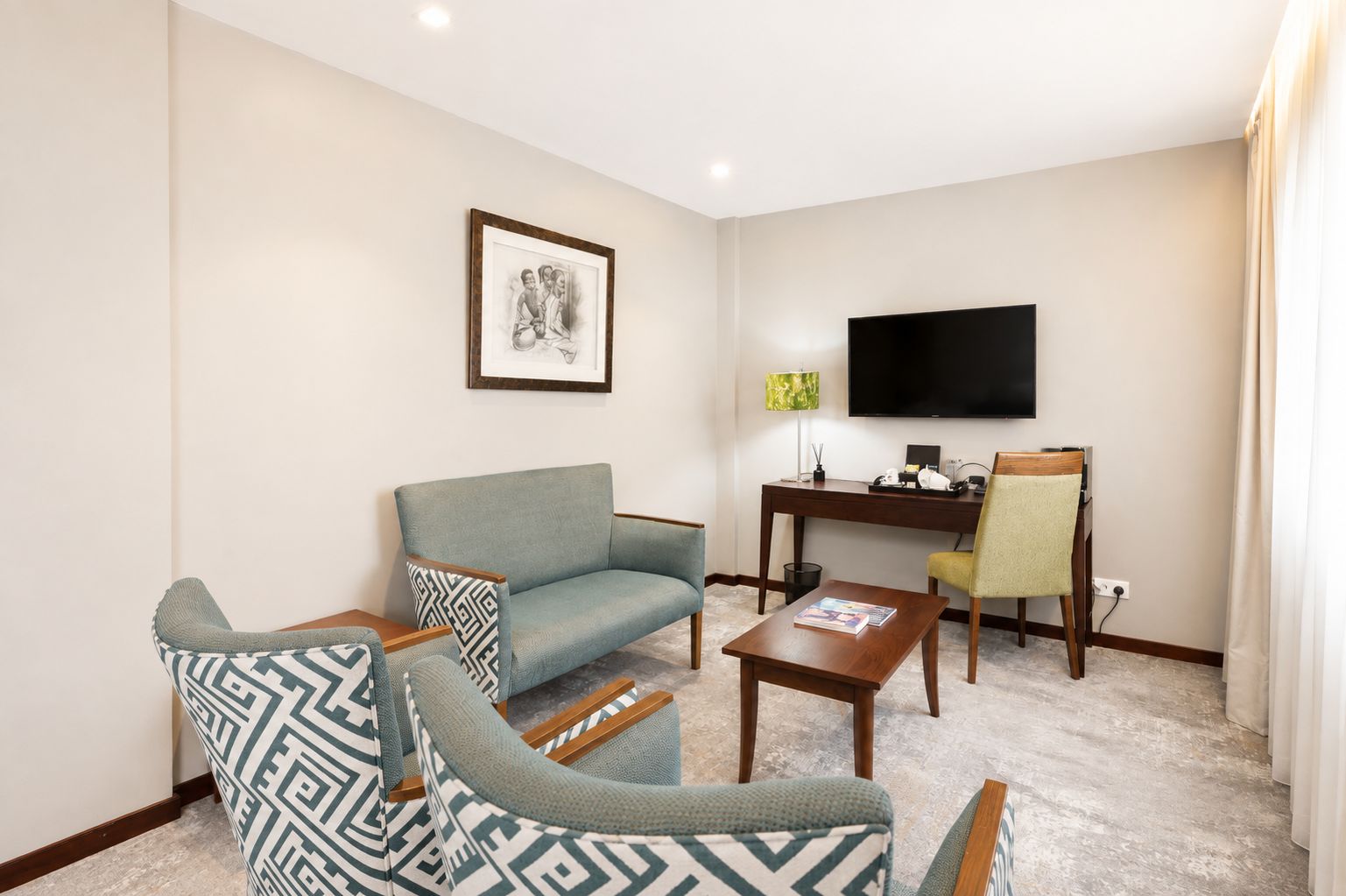 A living room with a sofa, armchair, coffee table, and a desk with a television.