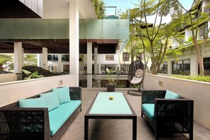 A modern outdoor seating area with wicker furniture and a central table, surrounded by greenery and a multi-level building structure. - Mercure Bali Legian (Legian)