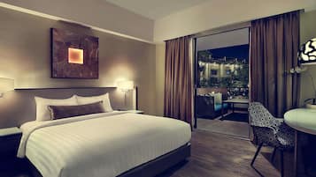 Habitación de hotel con una cama grande, un escritorio con silla, una mesita de noche, una lámpara de pared y vistas al exterior.