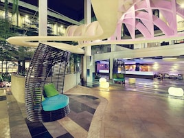 Un moderno vestíbulo de hotel con una zona de estar central, una recepción y una escalera que lleva a los pisos superiores.