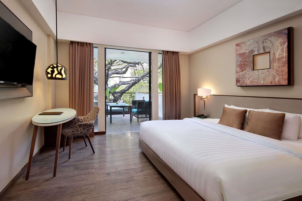 Habitación de hotel con cama, escritorio, silla, televisor, lámpara y vistas al exterior.