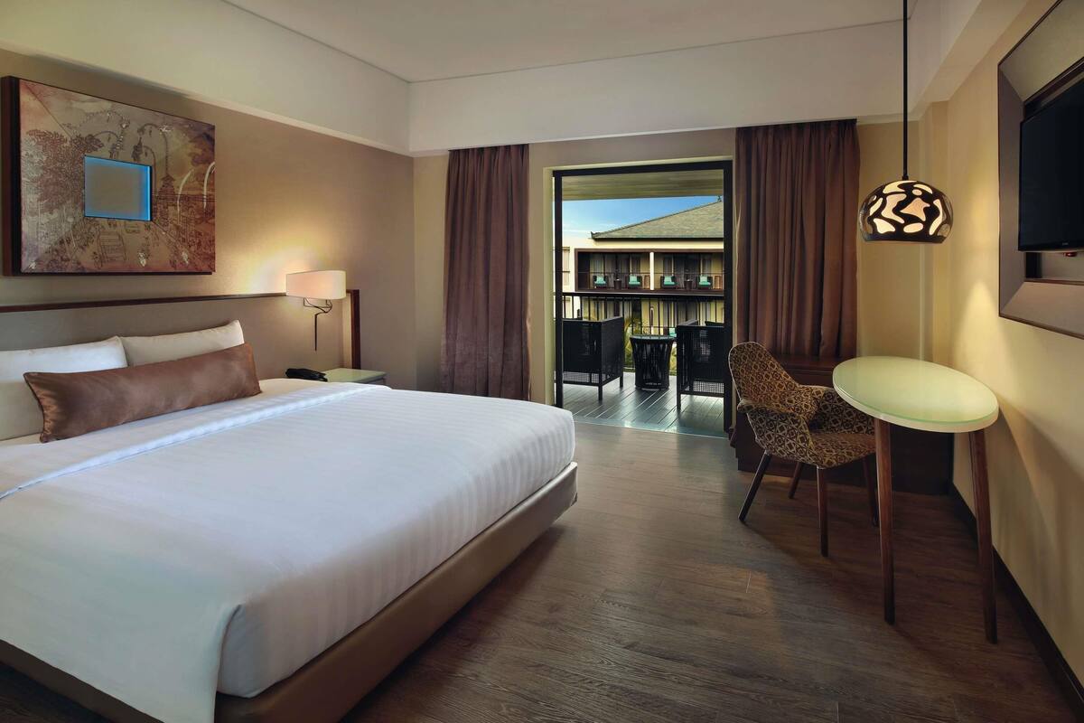 Habitación de hotel con una cama grande, una silla, una mesa, un televisor y vistas al exterior.