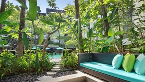 Un jardín con zona de estar, escalones que llevan a una piscina y abundante vegetación.