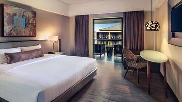 A hotel room with a large bed, a desk, a chair, a TV, and a balcony with a view.