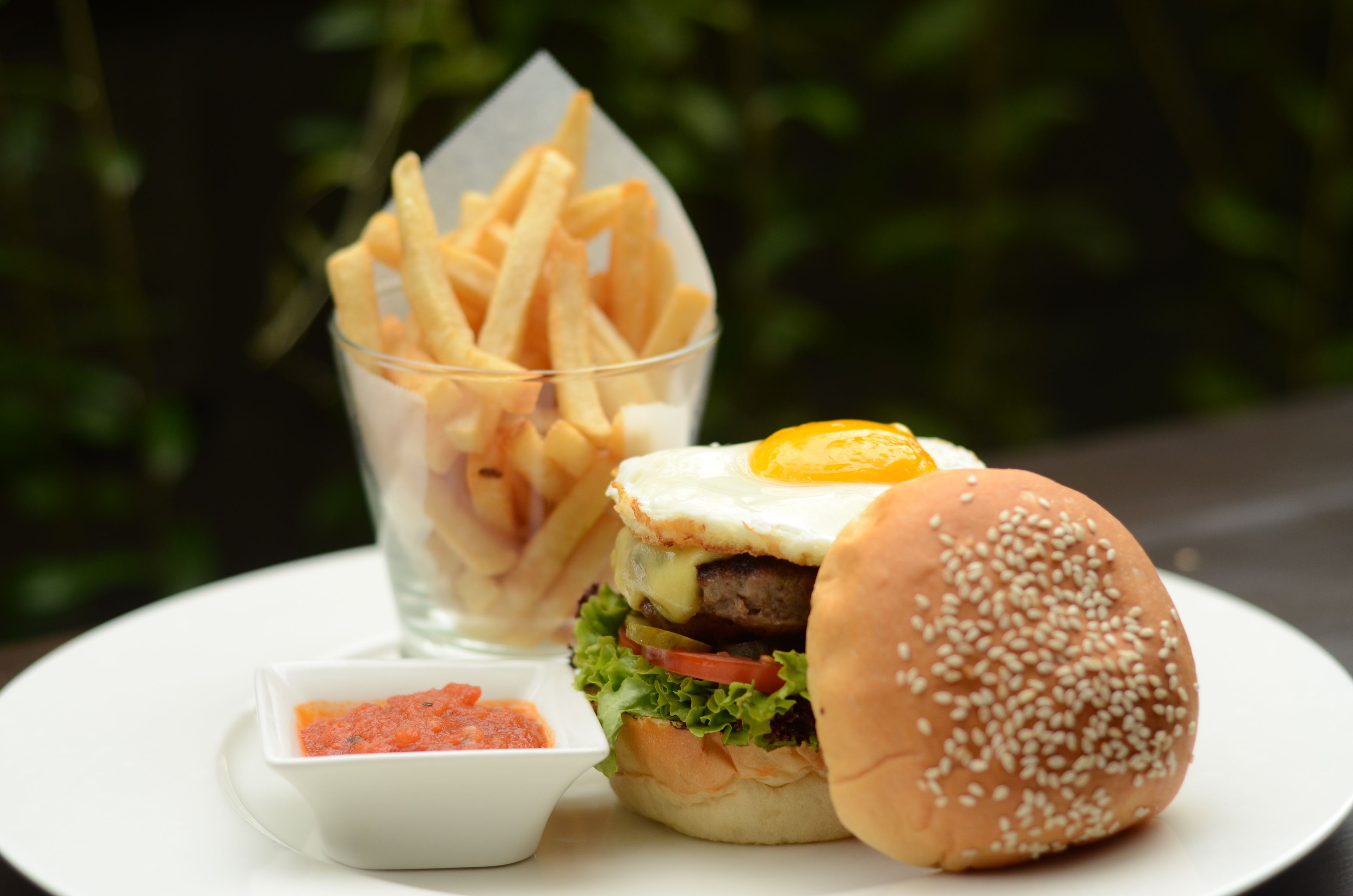 Un hamburger avec un œuf au plat sur le dessus, une portion de frites et un petit bol de ketchup.
