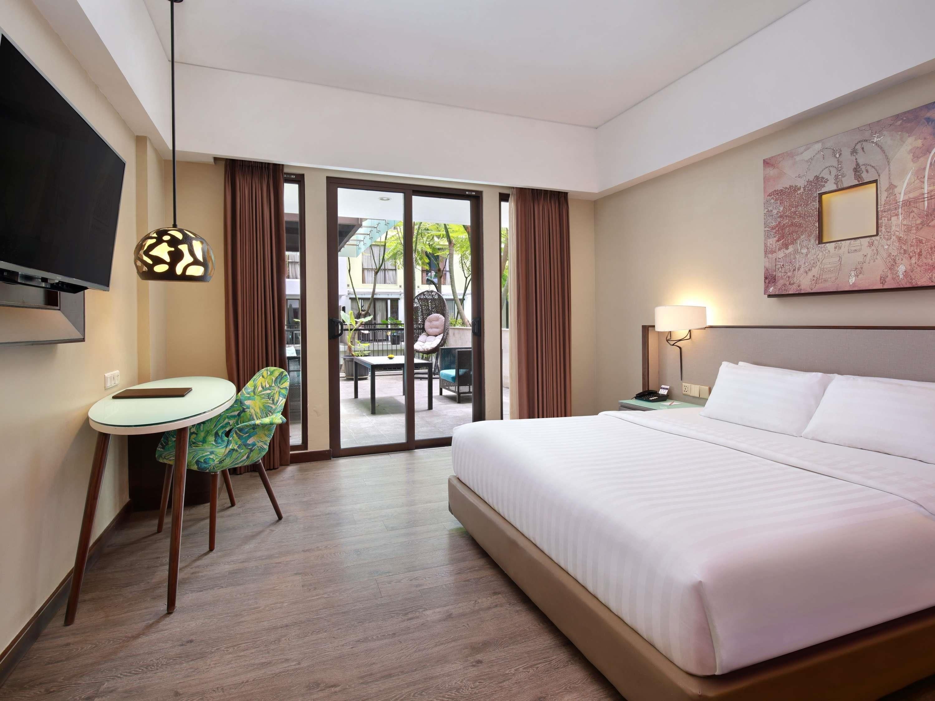 Habitación de hotel con cama, televisor, escritorio y silla, y vista al exterior.