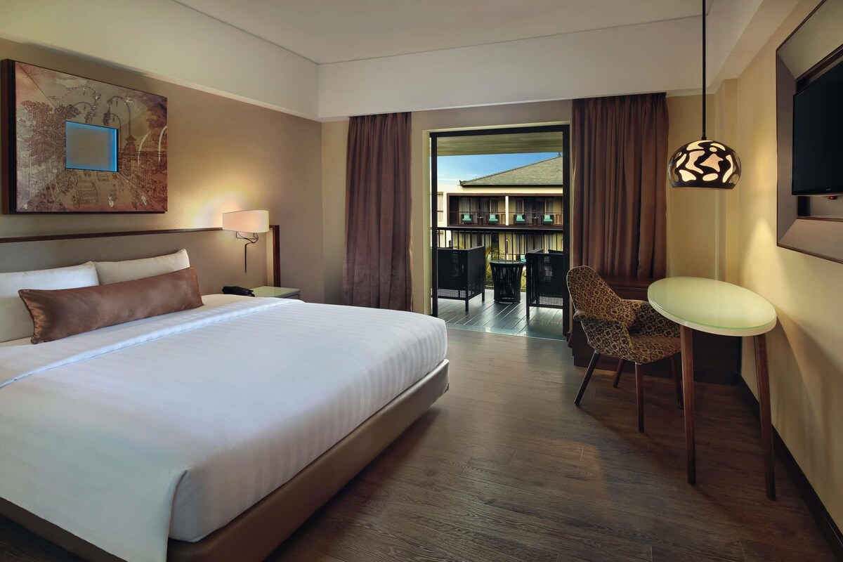 Habitación de hotel con una cama grande, una silla, una mesa, un televisor y vistas al exterior.