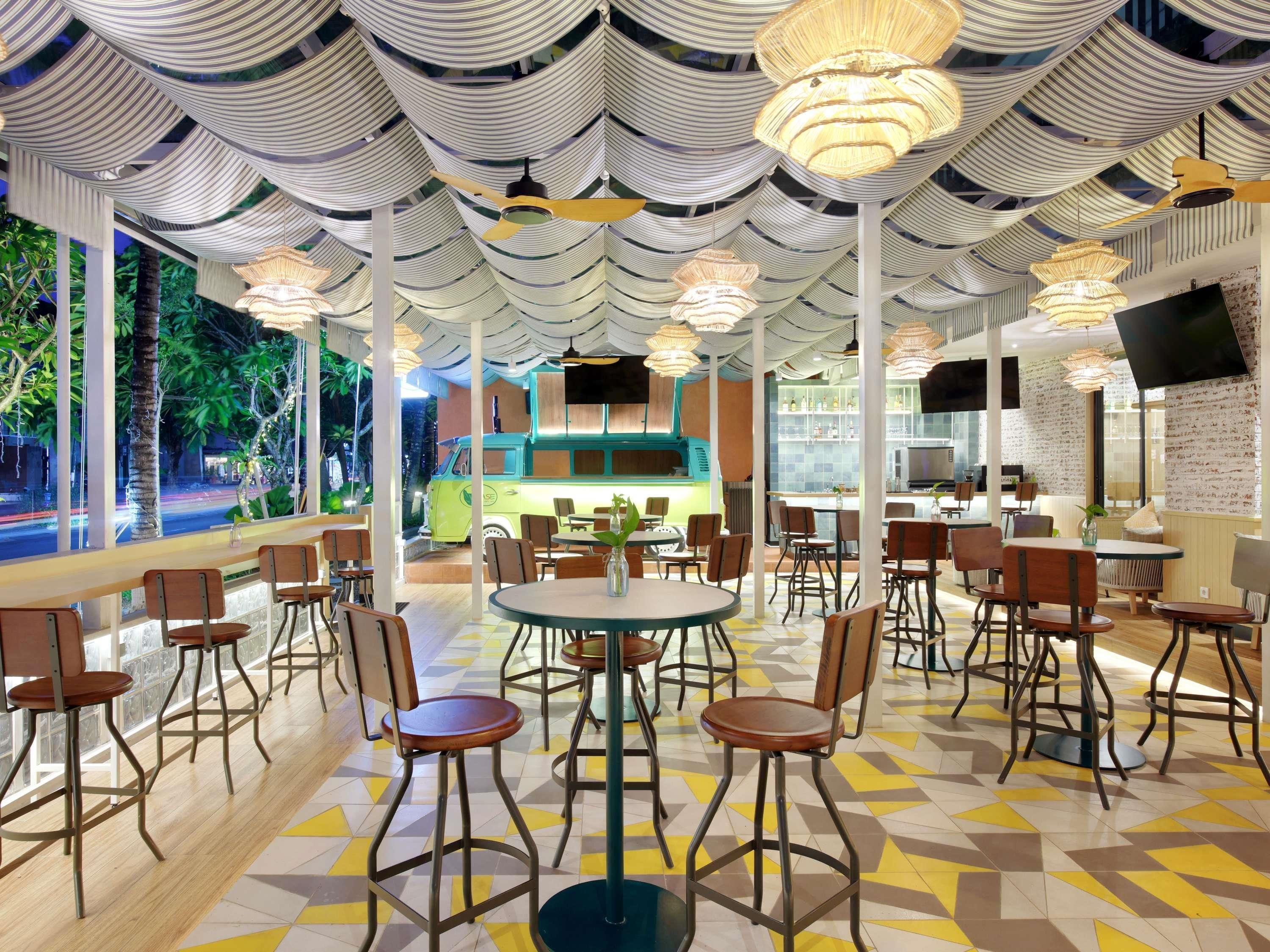 Un restaurante con un interior moderno, que presenta patrones de techo a rayas, mesas redondas y sillas de madera.