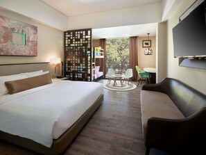 A hotel room with a bed, a seating area with a table and chairs, a TV, and a large window. - Mercure Bali Legian (Legian)