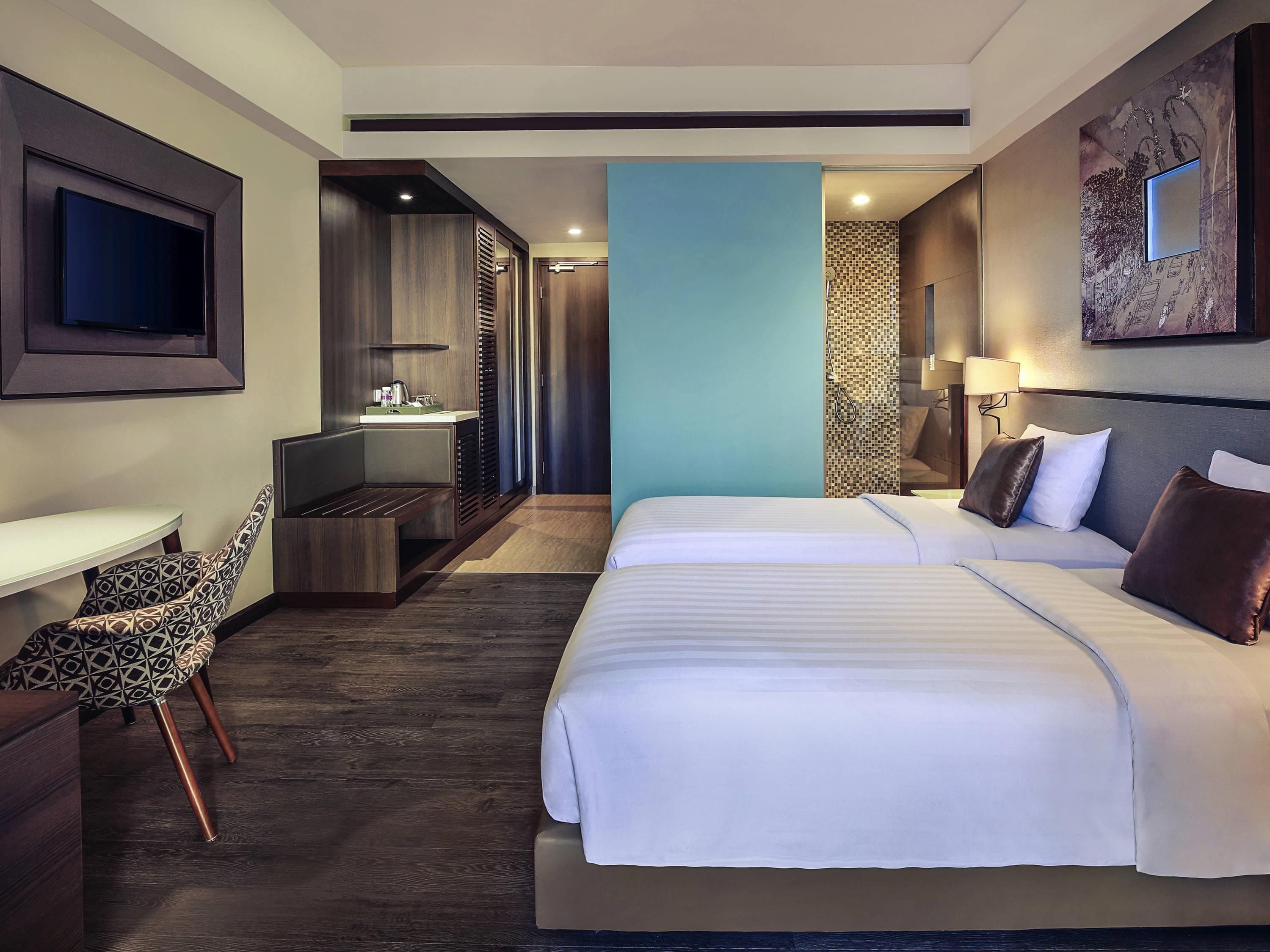 A hotel room with a large bed, a desk with a chair, a TV mounted on the wall, and a shower area.