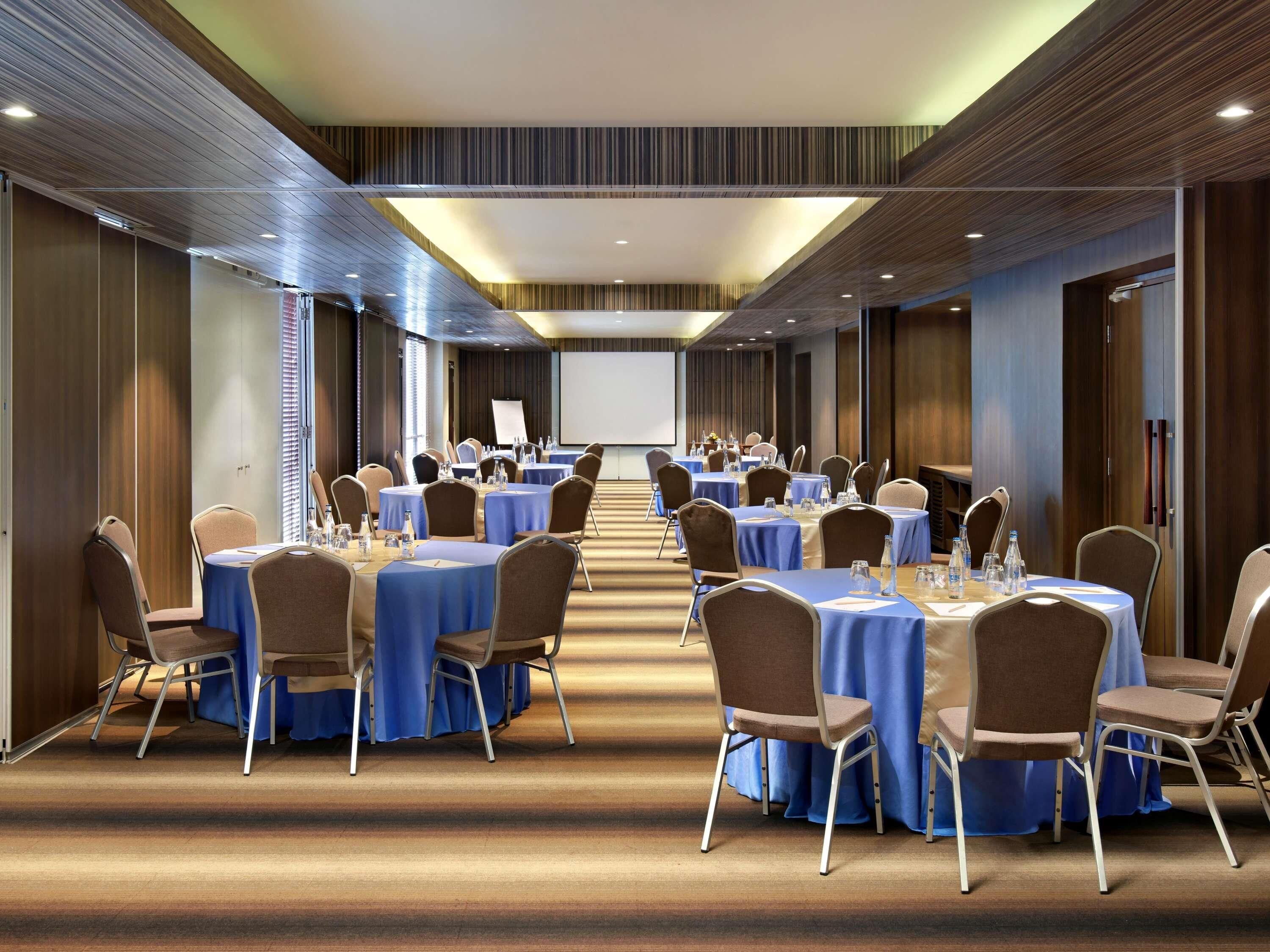A conference room with round tables, chairs, and a projector screen.