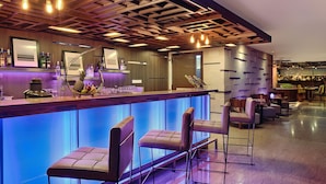Zona de bar con diseño moderno, que incluye un techo de madera, taburetes y una barra con botellas y vasos.
