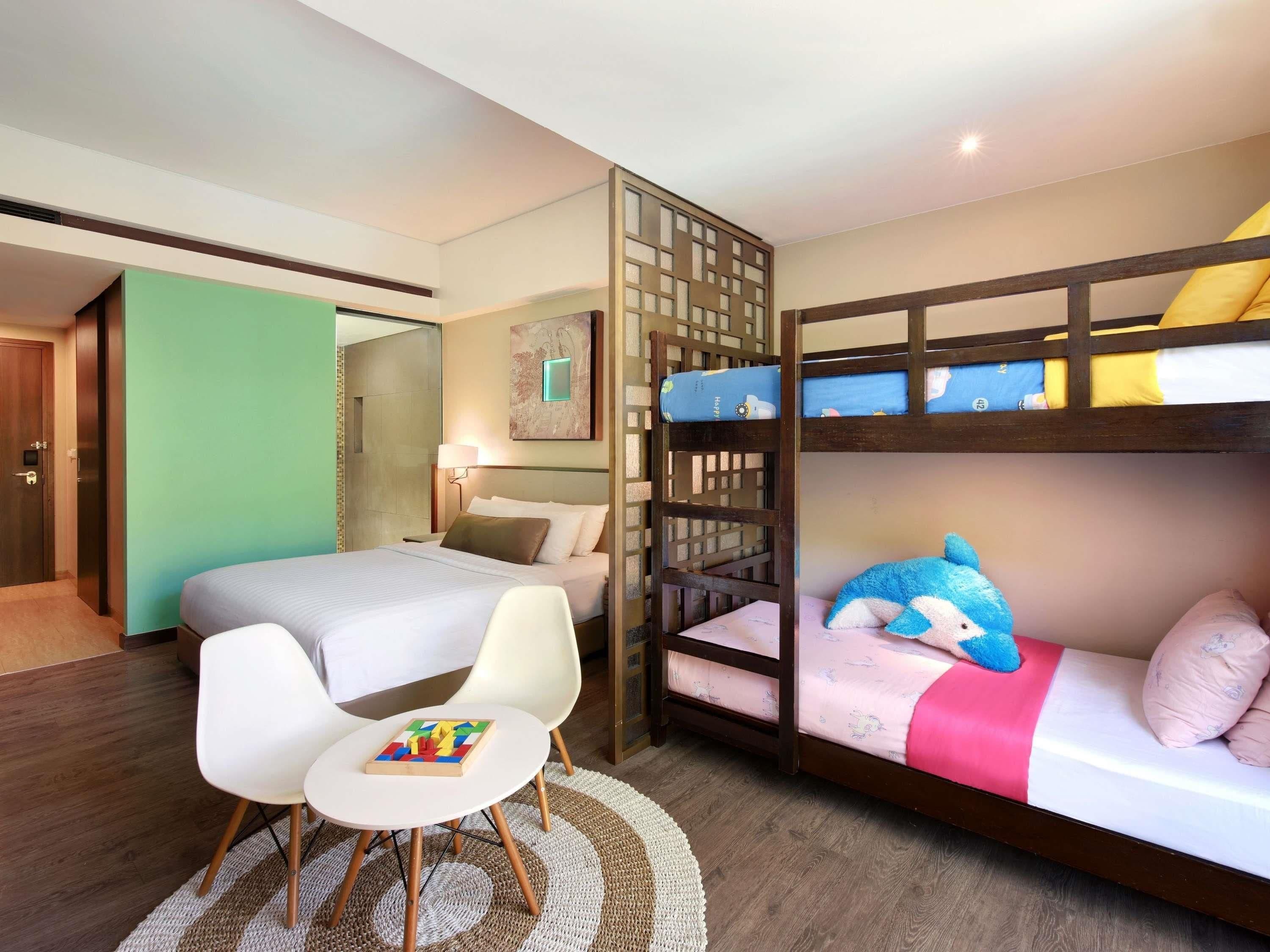 A hotel room with a bunk bed, a single bed, a desk with a chair, and a small rug.