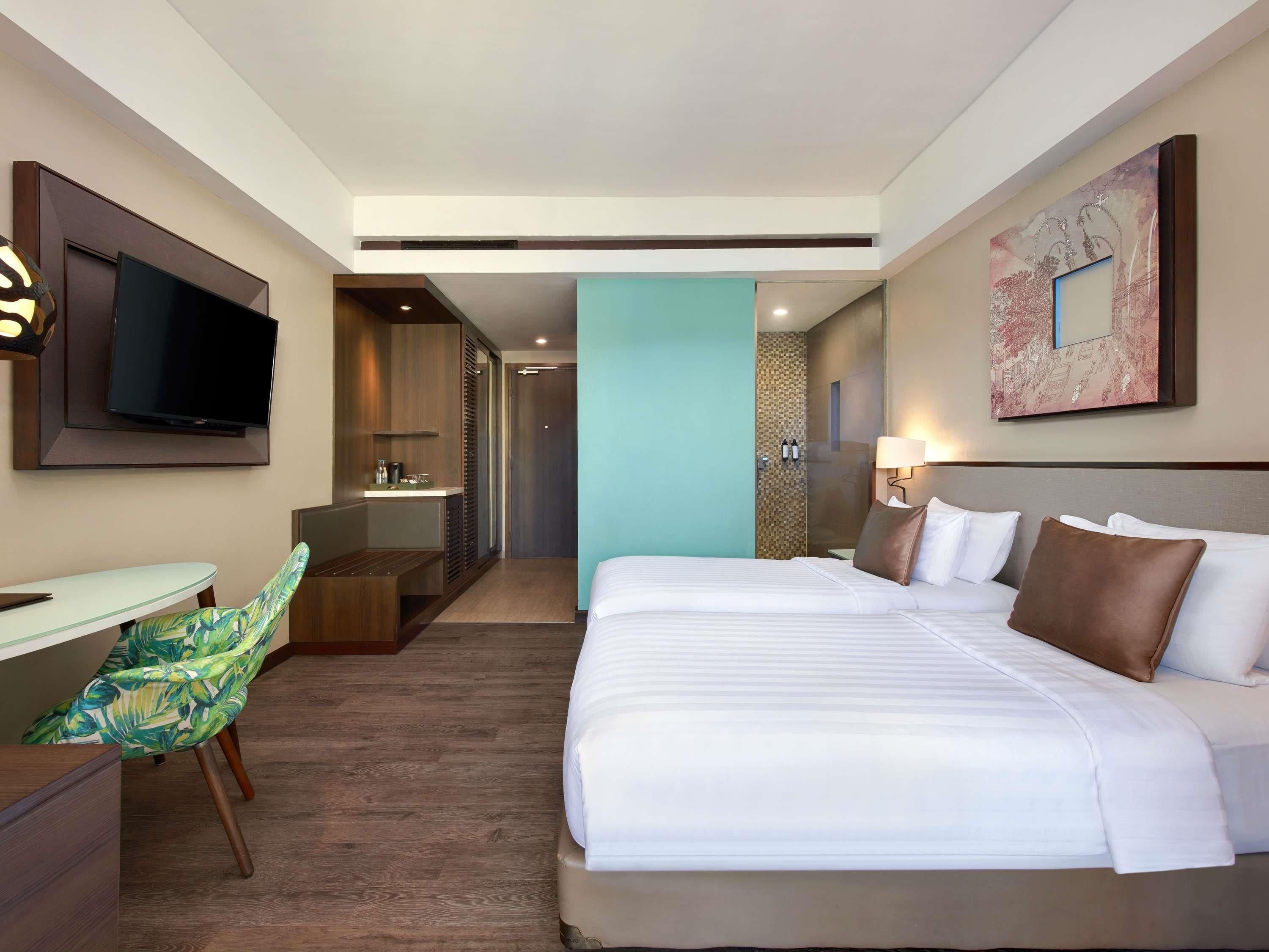 Habitación de hotel con cama, escritorio con silla, televisor, baño y un cuadro en la pared.