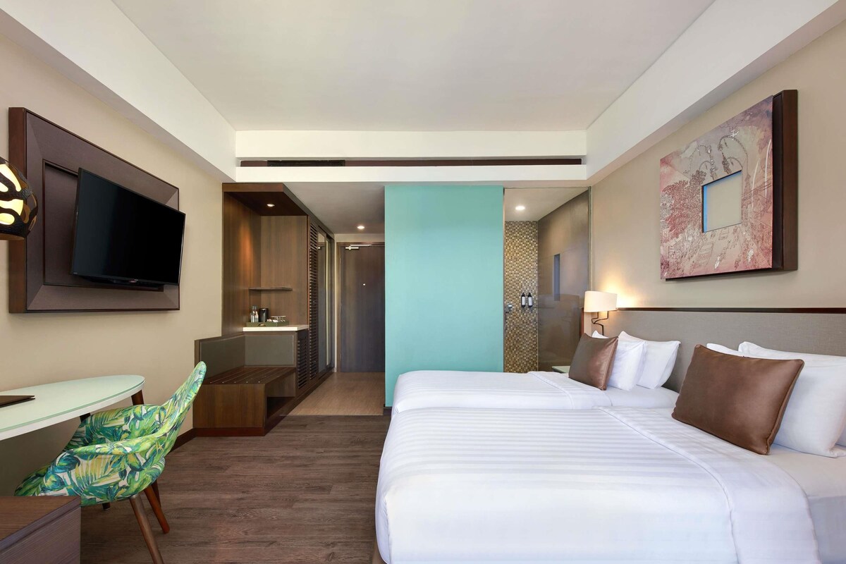 Habitación de hotel con cama, escritorio con silla, televisor, baño y un cuadro en la pared.