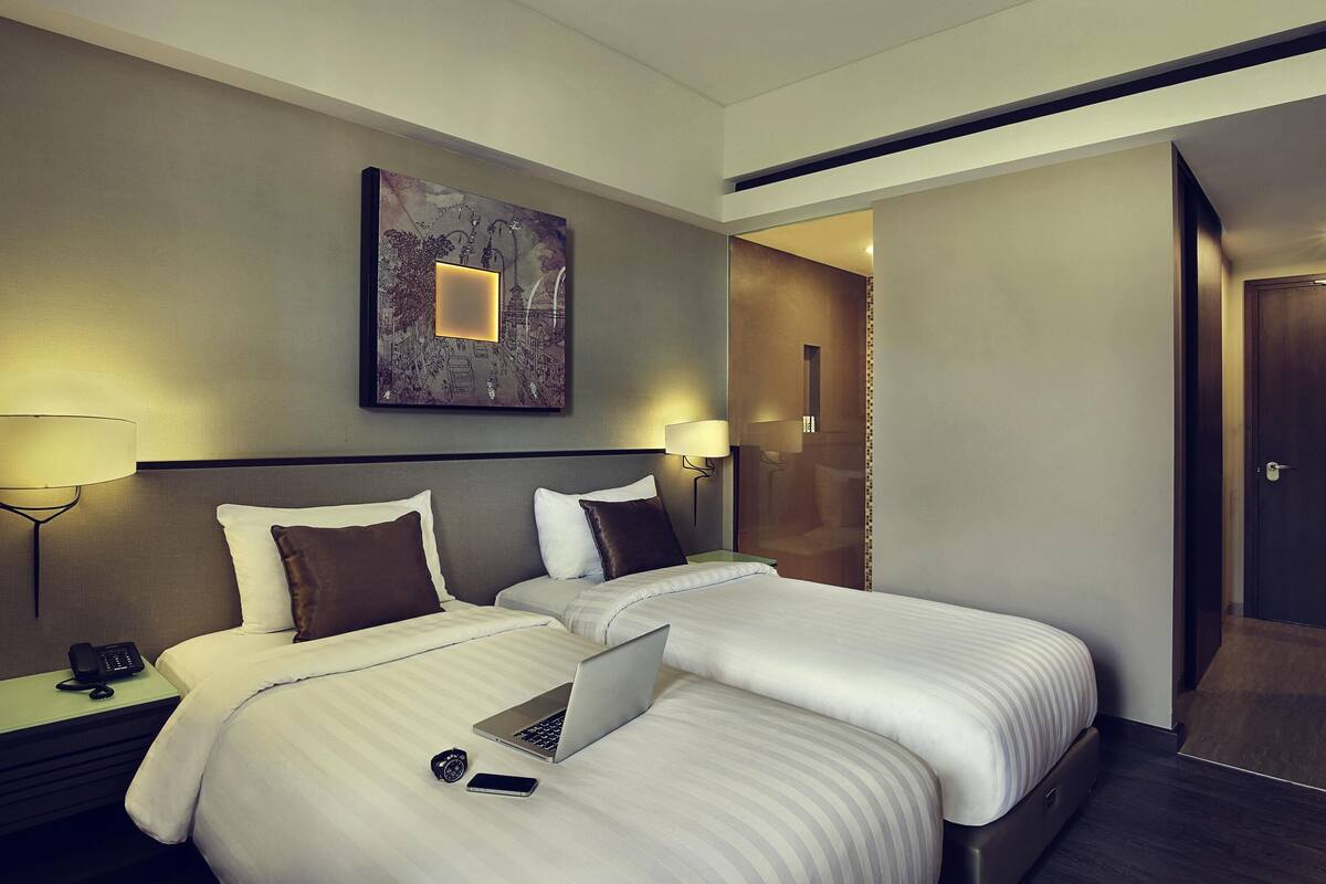 Habitación de hotel con dos camas, un escritorio con una computadora portátil, un teléfono y una mesita de noche con un teléfono.