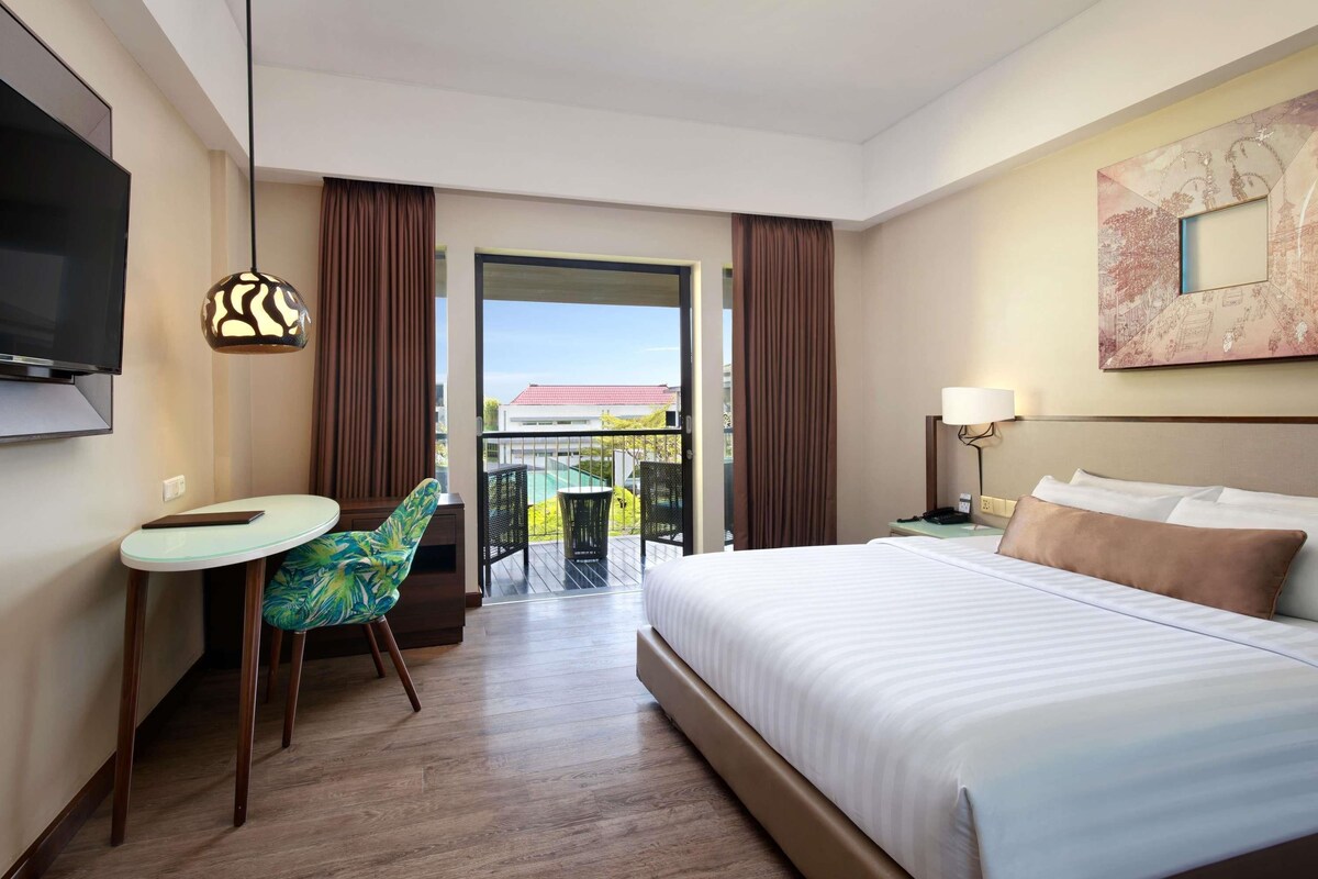Habitación de hotel con cama, televisión, escritorio con silla y balcón con vista a la piscina.
