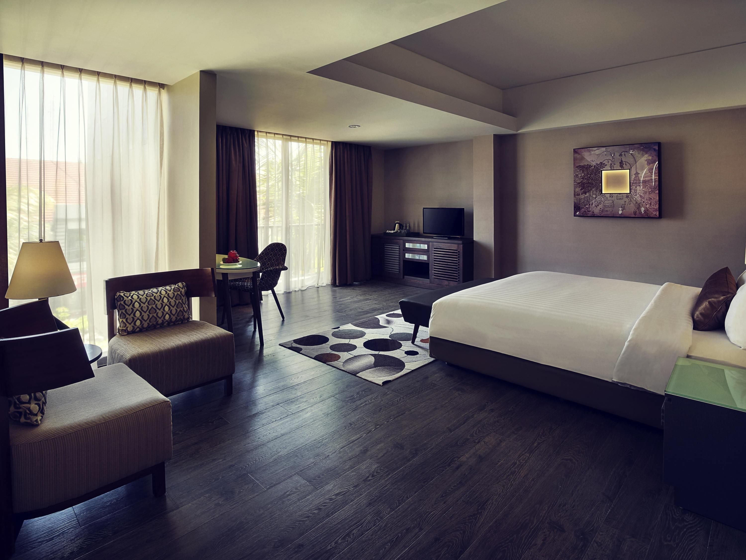 A modern hotel room with a large bed, a desk with a chair, a TV, and a painting on the wall.