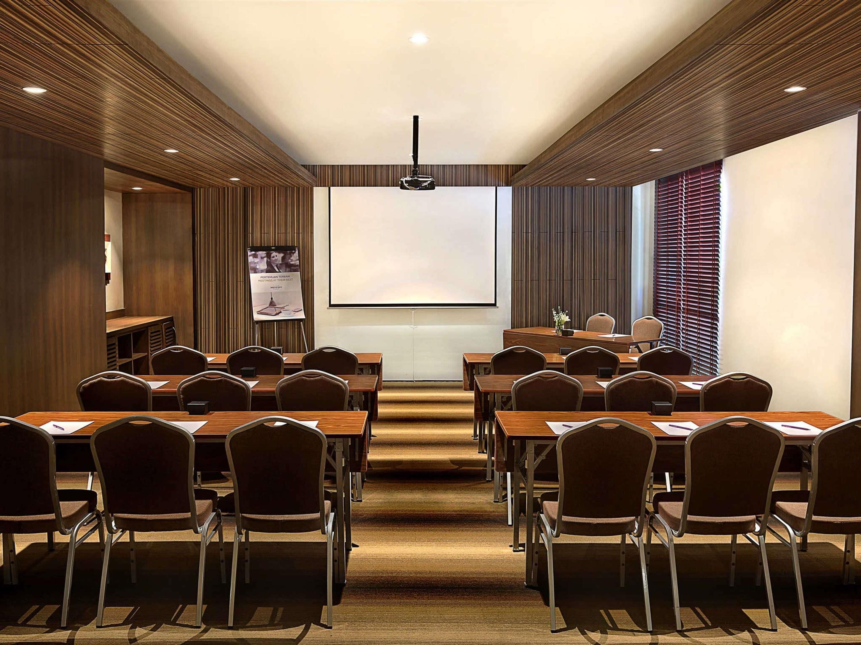 A conference room with wooden paneling, a projector screen, and rows of chairs.
