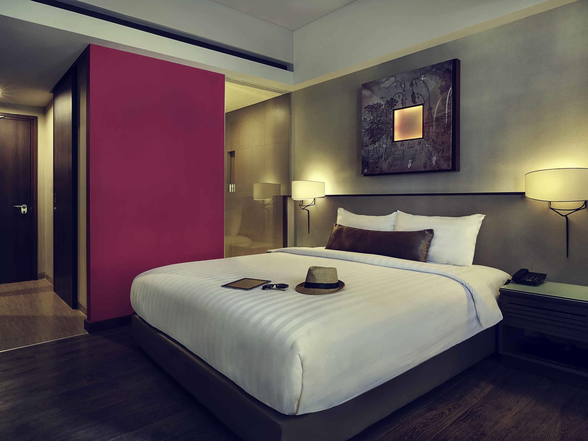 A hotel room with a large bed, bedside lamps, a nightstand, a phone, a hat, and a tablet on the bed.