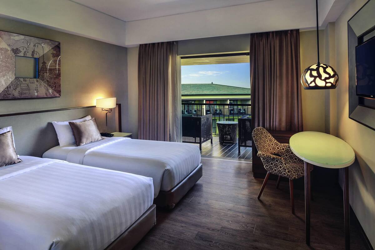 Habitación de hotel con dos camas, un escritorio, una silla, un televisor y un balcón con vistas.