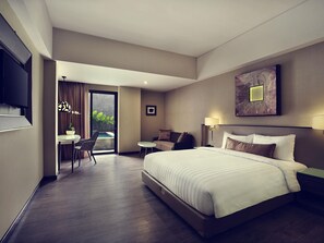 A hotel room with a large bed, a desk, a chair, a sofa, a television, and a painting on the wall. - Mercure Bali Legian (Legian)