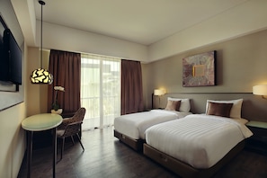 A hotel room with two beds, a desk, a chair, a TV, and a window with curtains. - Mercure Bali Legian (Legian)
