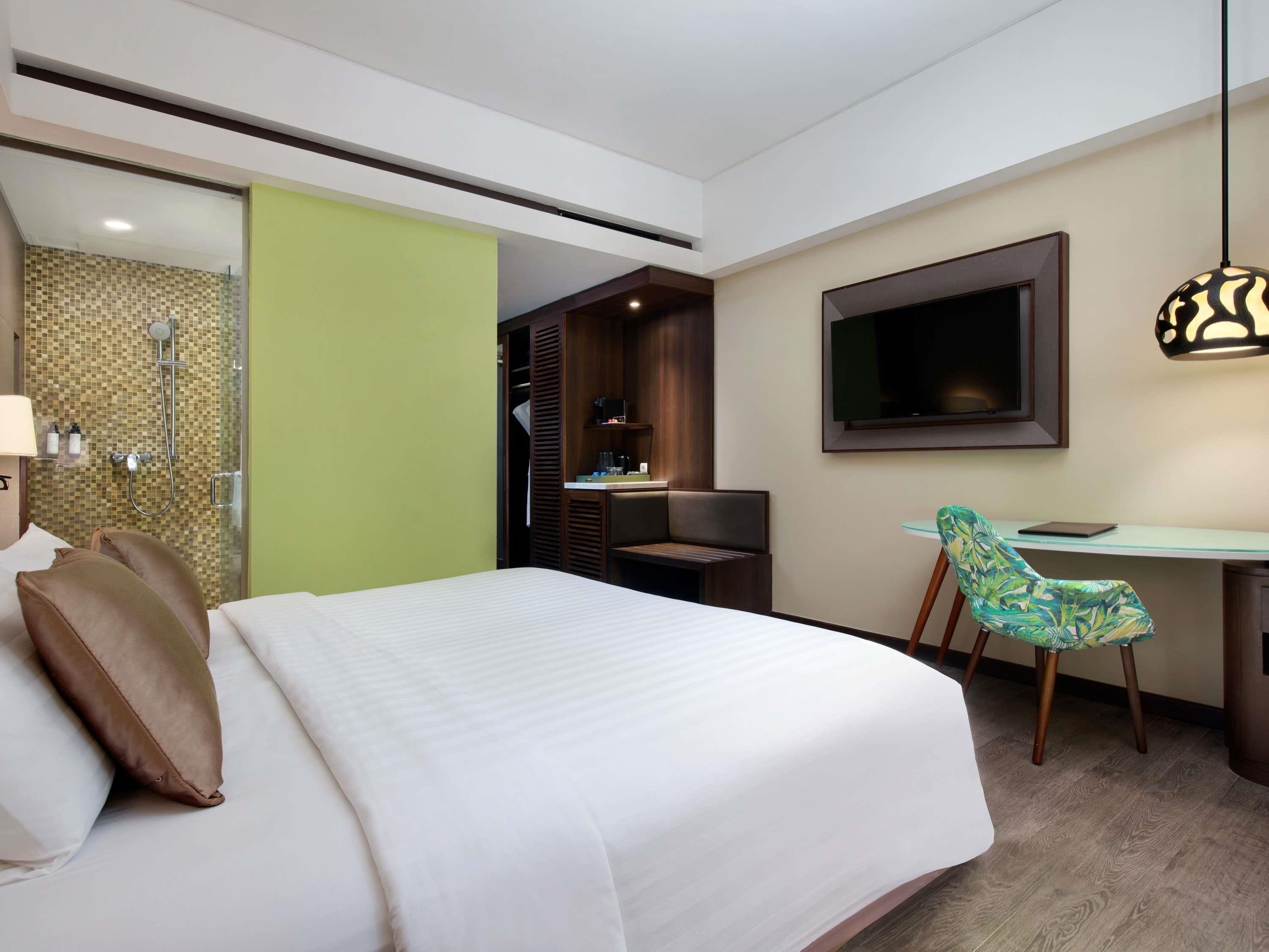Habitación de hotel con cama, escritorio, televisión y zona de ducha.