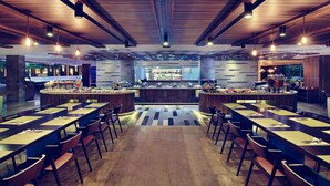 Un comedor amplio con mesas y sillas largas, una zona de bar central y un diseño de techo moderno.