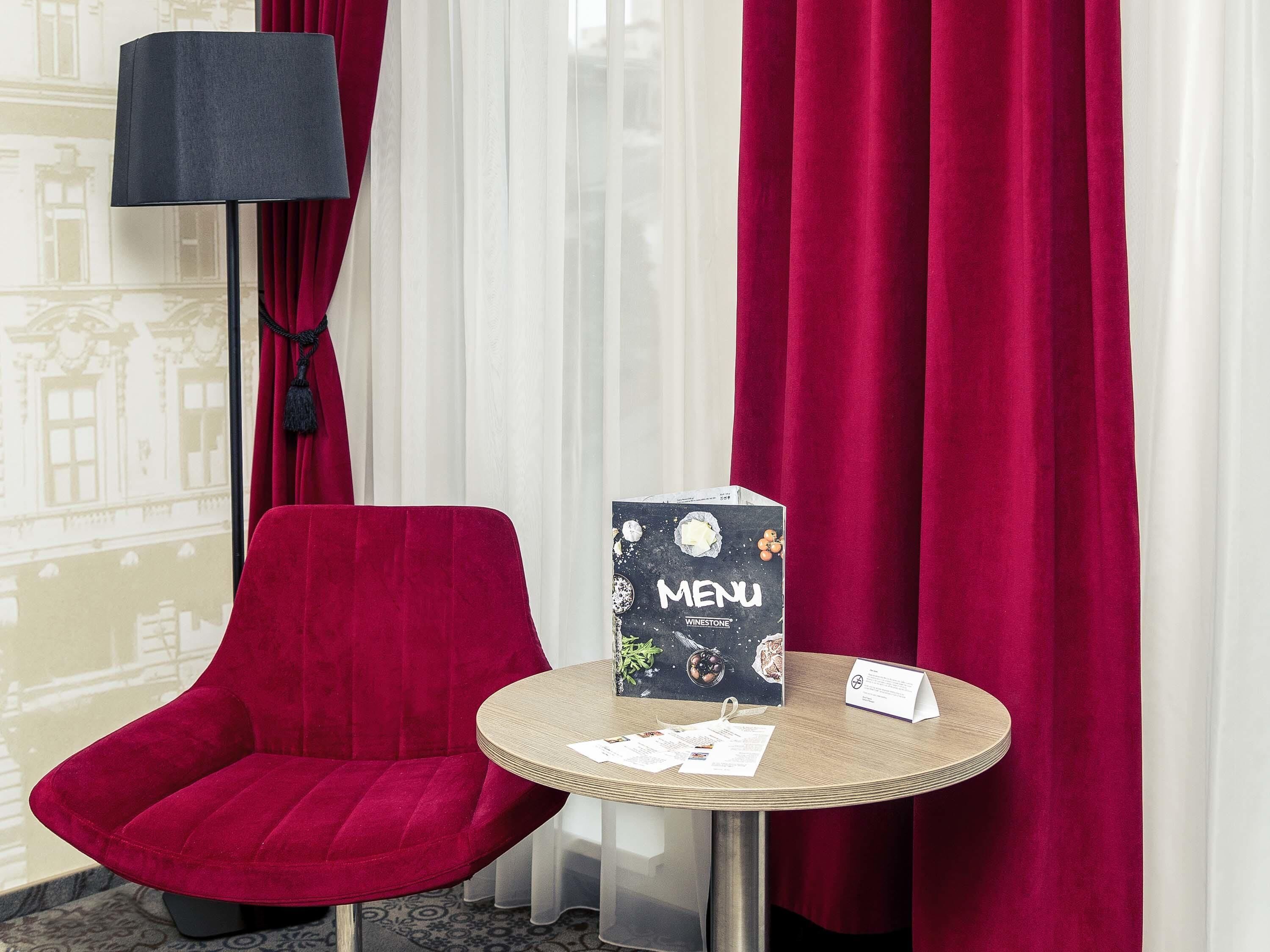 A red velvet chair, a round table with a menu, and a lamp in a hotel room.