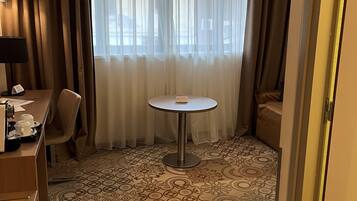 Una habitación de hotel con una mesa redonda, una silla, un escritorio con lámpara y una alfombra estampada.