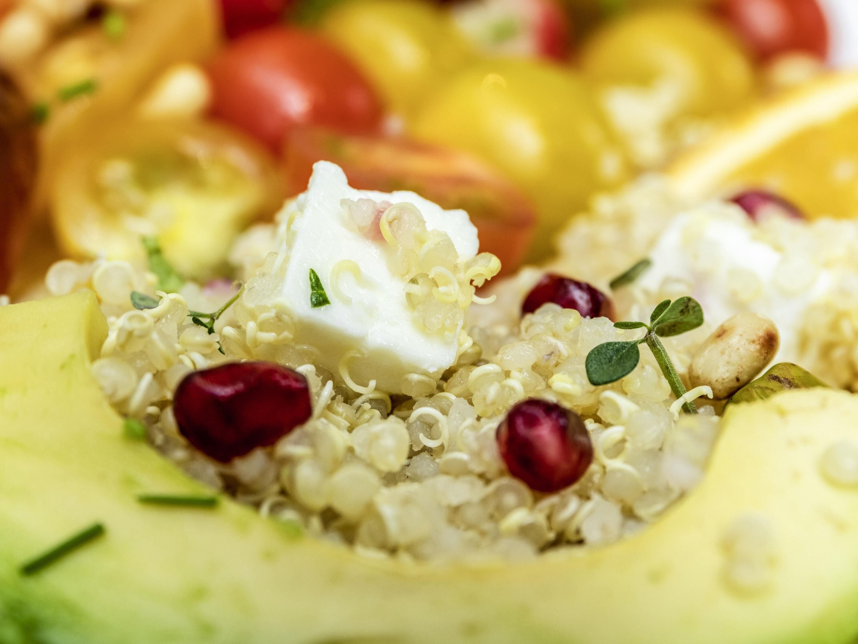 A close-up of a salad with quinoa, feta cheese, pomegranate seeds, and avocado slices.