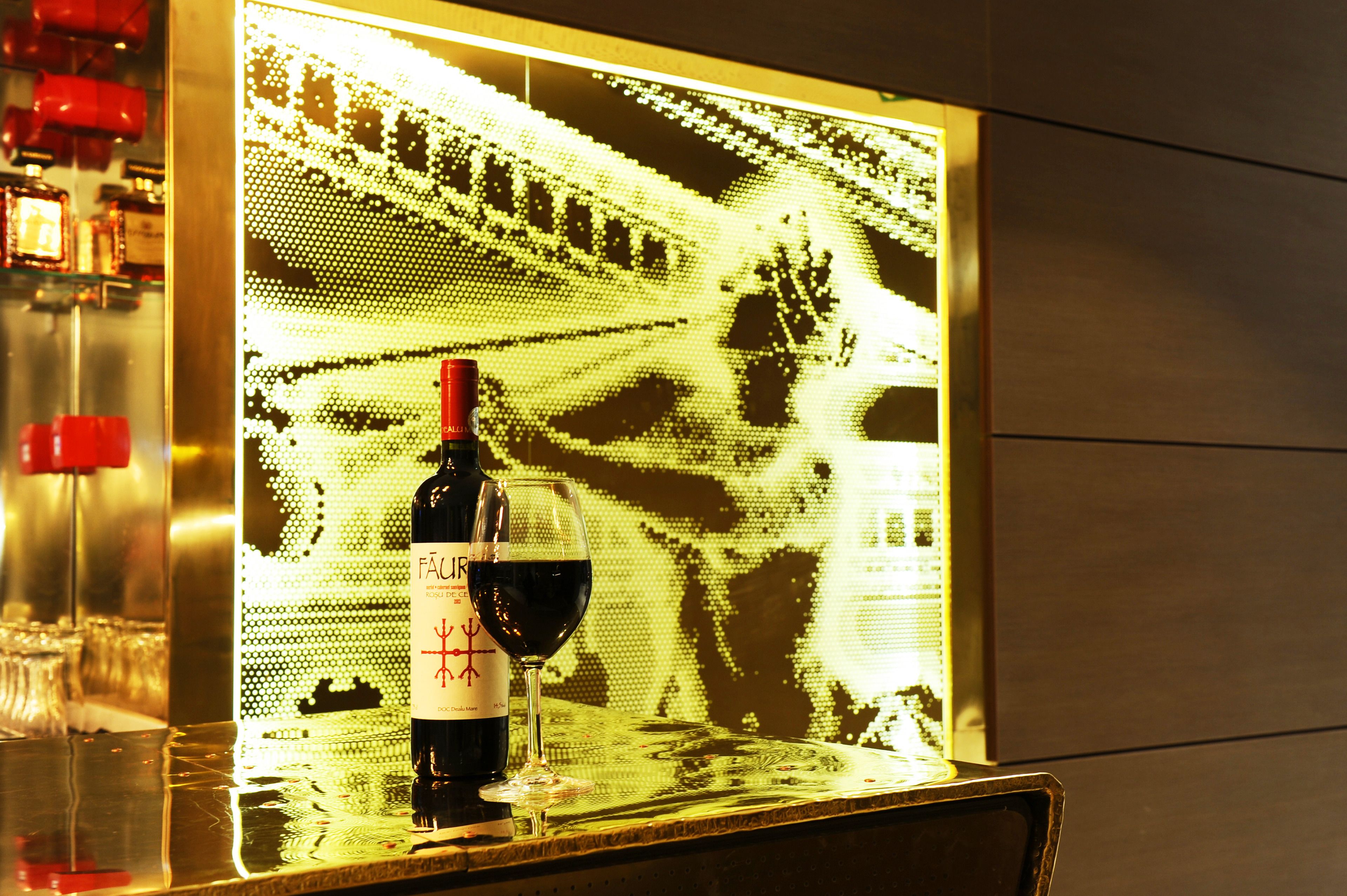 A bottle of wine and a glass on a reflective surface with a digital display in the background.
