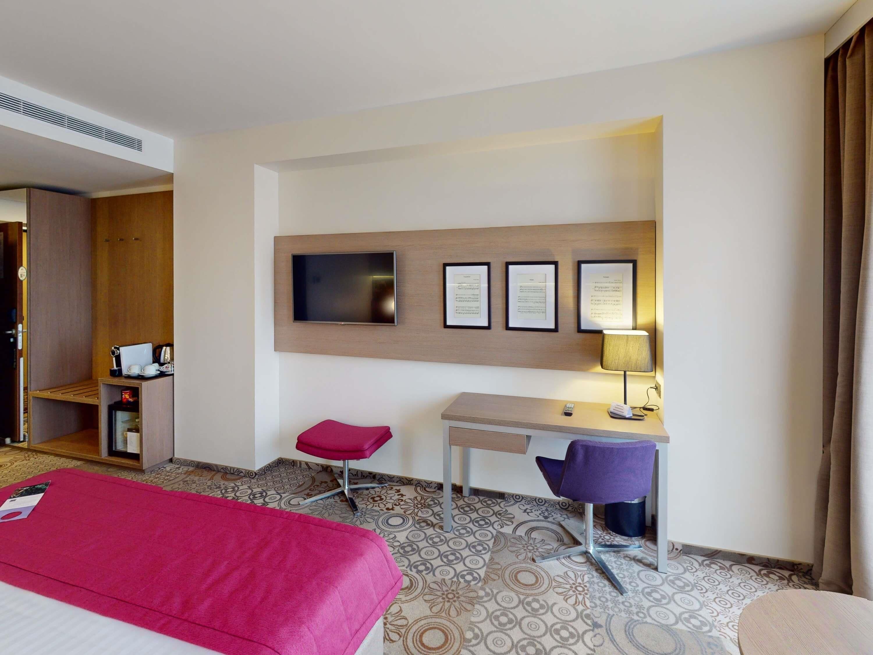 A hotel room with a bed, a desk, a chair, a television, and a lamp.