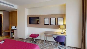 A hotel room with a bed, a desk, a chair, a television, and a lamp.