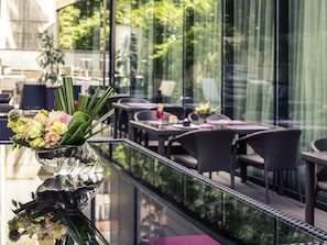 A glass railing with a flower arrangement, outdoor seating, and a view of greenery through the glass. - Mercure Bucharest City Center (Bucharest)