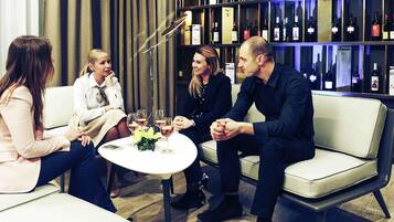 A group of people seated around a table with wine glasses, in a room with a wine rack in the background.