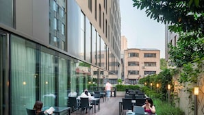 Een terras met tafels en stoelen, omringd door gebouwen en groen.