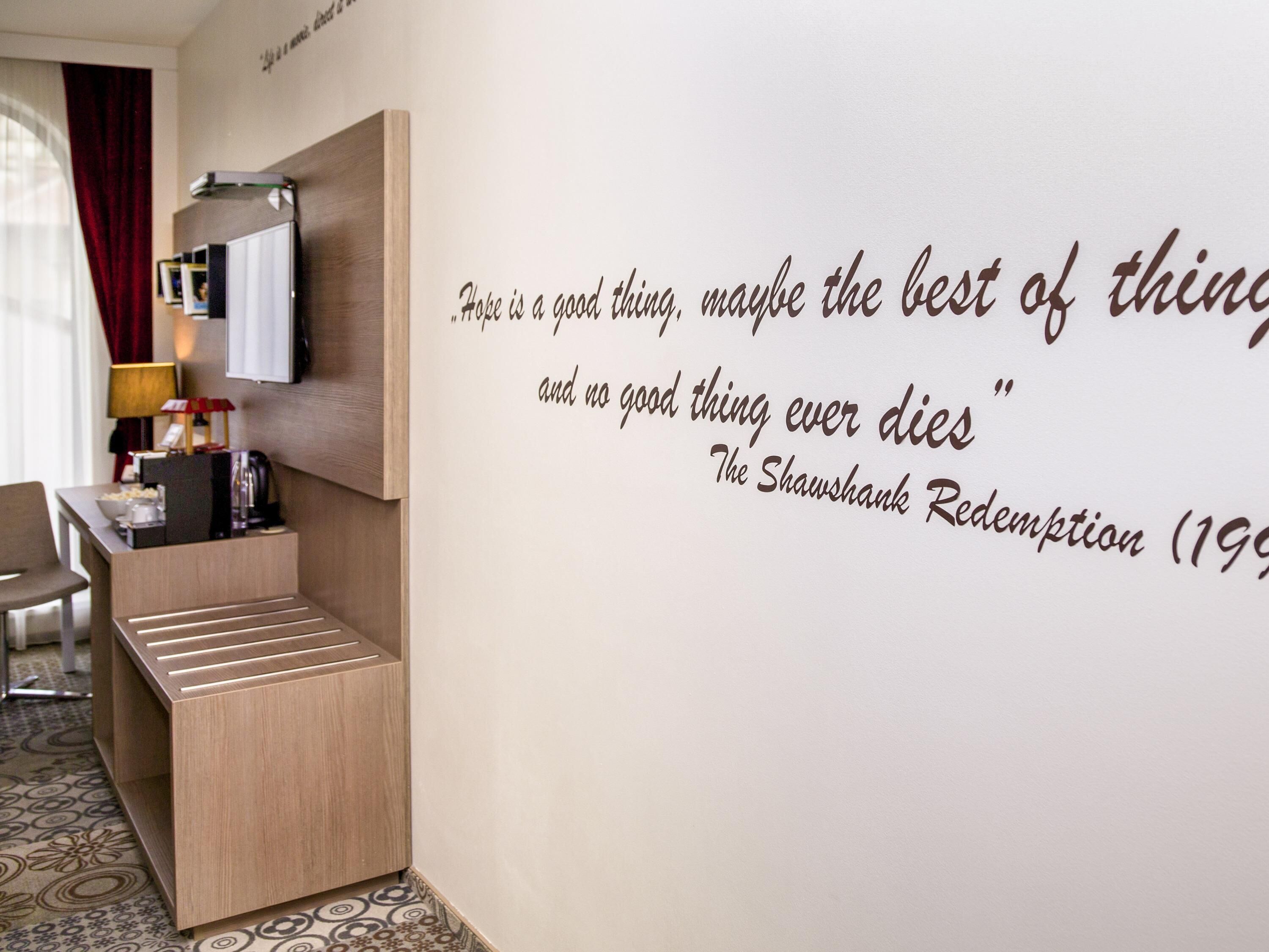 Una habitación de hotel con una cita en la pared, un escritorio con lámpara y una silla.