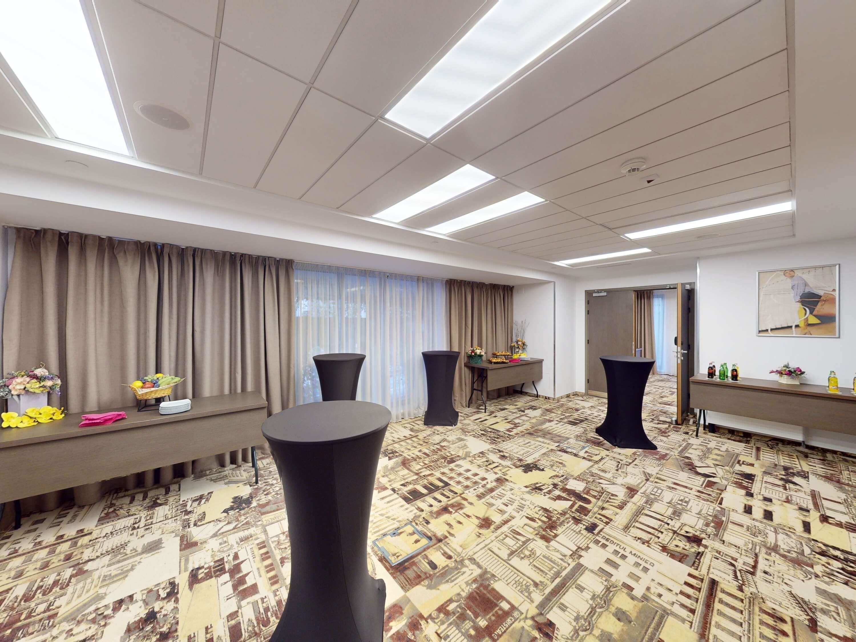 Habitación de hotel con una cama grande, un escritorio con computadora, una silla, una ventana con cortinas y una alfombra estampada.