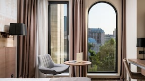 Hotelkamer met een bed, een bureau, een stoel, een laptop op een bijzettafeltje en een groot raam met gordijnen.