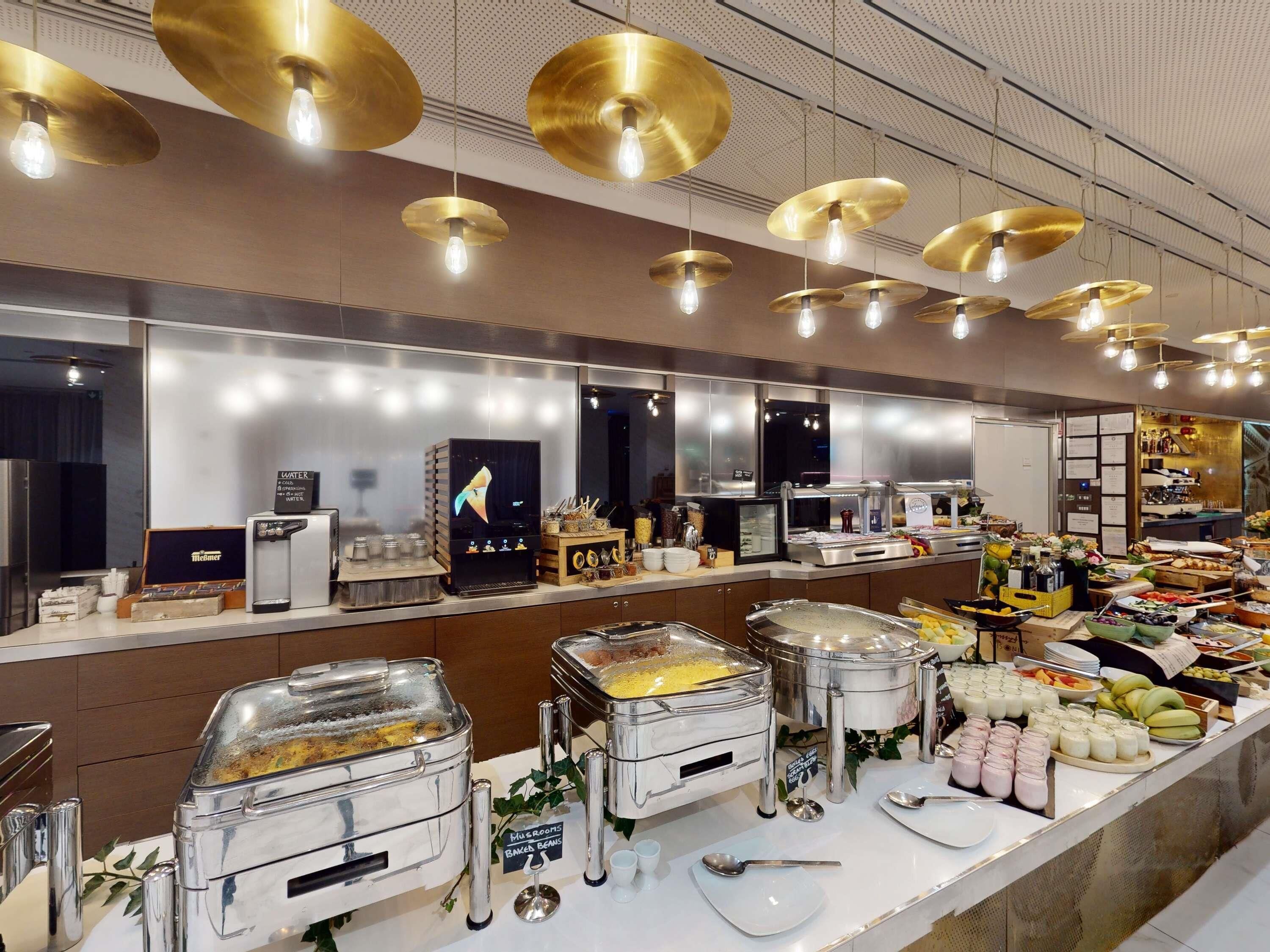 Un espace buffet avec différents stands de nourriture, notamment une machine à café et un panneau indiquant les plats à base de champignons et de haricots cuits.